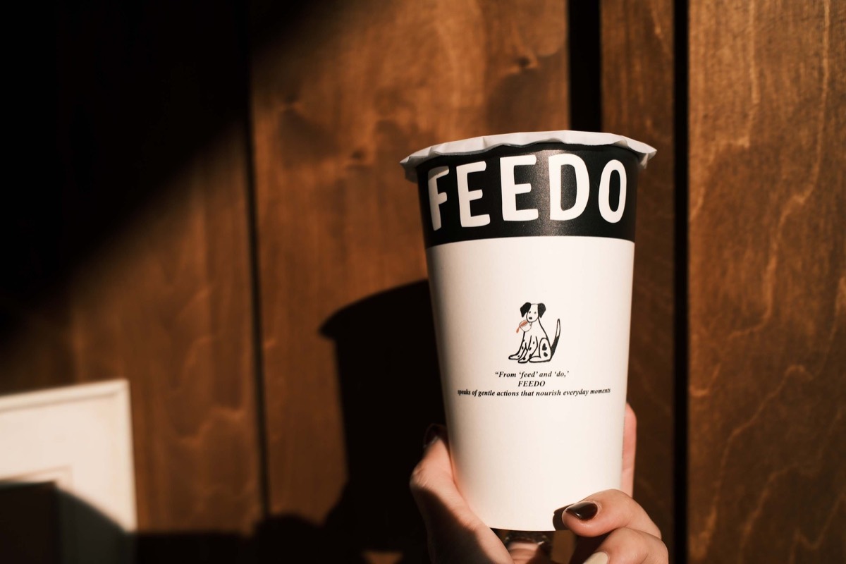 手拿一杯 FEEDO 茶飲，午後的光照在杯身上